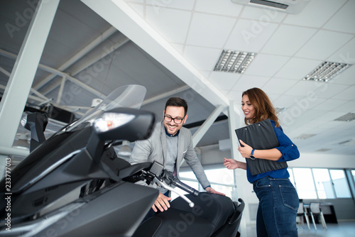 Man buying a new motorcycle at vehicle dealership showroom with help of an attractive saleswoman.