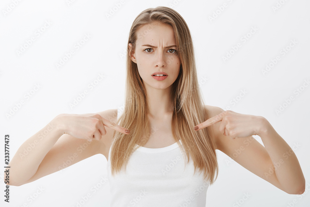 Intense girl with serious face pointing at herself as asking question, concerned and unsure frowning making grimace waiting for friend tell opinion about her outfit posing over gray background Intense girl with serious face pointing at herself as asking question, concerned and unsure frowning making grimace waiting for friend tell opinion about her outfit posing over gray background