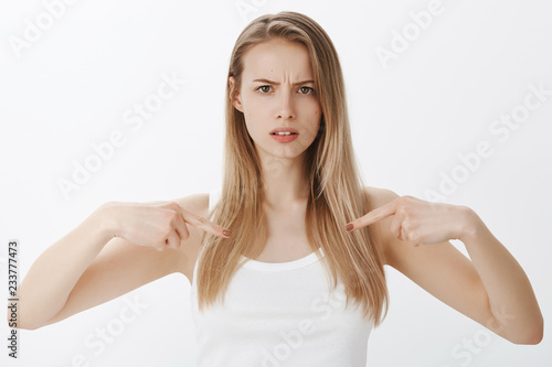 Intense girl with serious face pointing at herself as asking question, concerned and unsure frowning making grimace waiting for friend tell opinion about her outfit posing over gray background