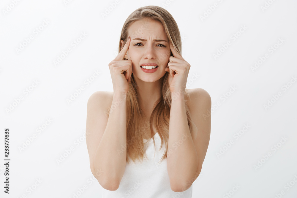 Portrait of troubled uneasy young female student being under pressure clenching teeth, frowning and squinting, touching temples as trying focus or remember important thing slipped mind over gray wall Portrait of troubled uneasy young female student being under pressure clenching teeth, frowning and squinting, touching temples as trying focus or remember important thing slipped mind over gray wall