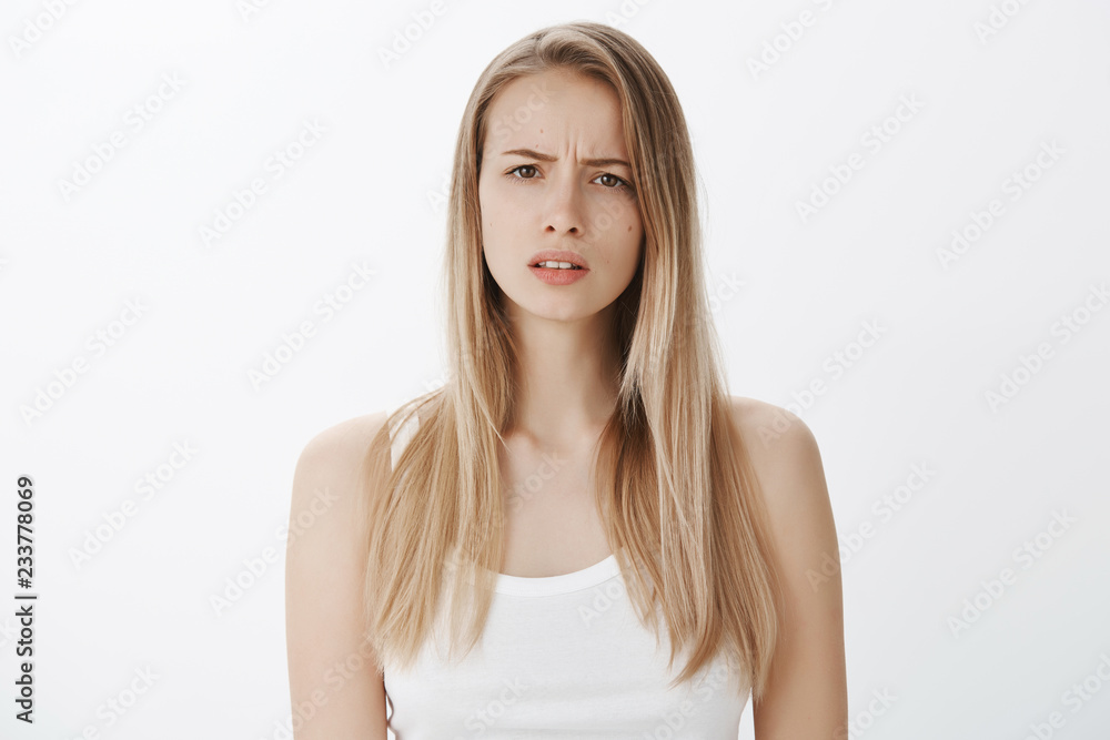 Portrait of confused puzzled attractive european female model with blond hair frowning and squinting as cannot get clue, standing questioned and clueless against gray background Portrait of confused puzzled attractive european female model with blond hair frowning and squinting as cannot get clue, standing questioned and clueless against gray background