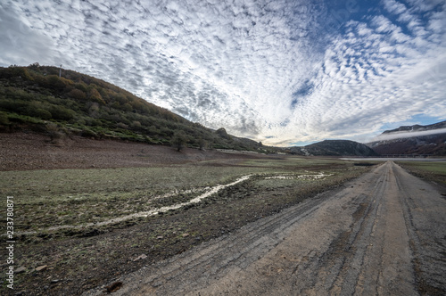 Old road in ruins that is generally flooded by the waters of the reservoir of Riaño in Leon, Spain. In the background you see the mountains between the morning mists.  photo