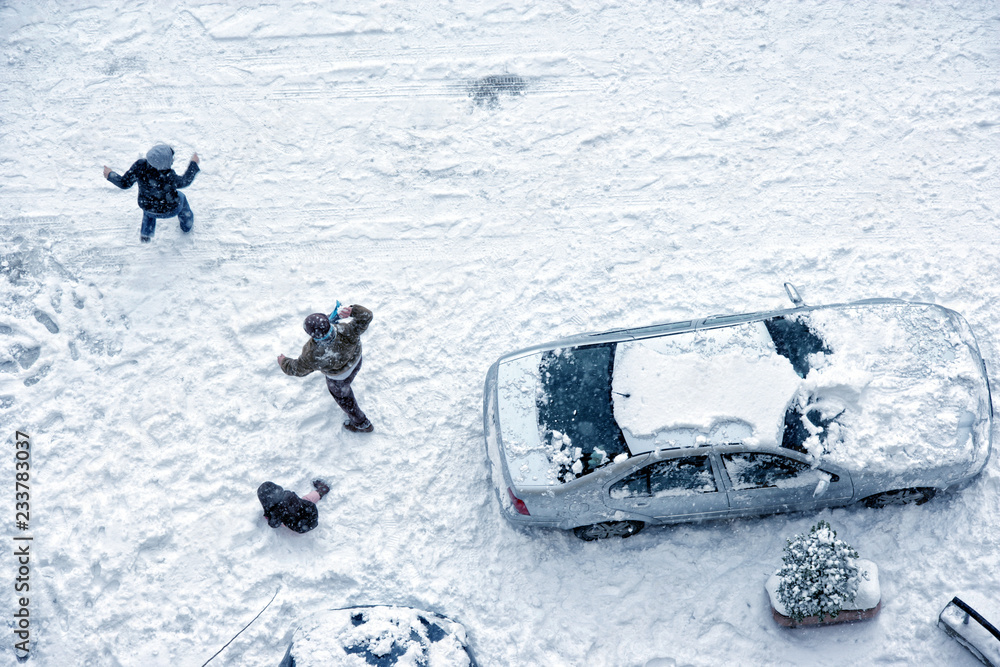 Naklejka premium Family play in snow around cars in parking lot