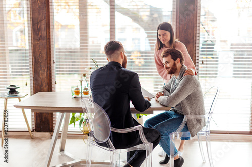 Tablou pe pânză Successful lawyer giving consultation to a young attractive family couple about in his modern office, buying renting apartment or house