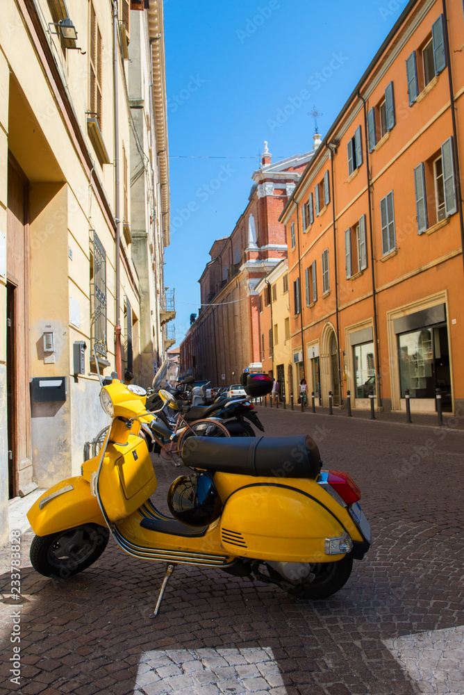 Yellow old fashioned scooter on street in Rimini with many-coloured houses, ancient city center. Vacation in beautiful Italy, Europe.