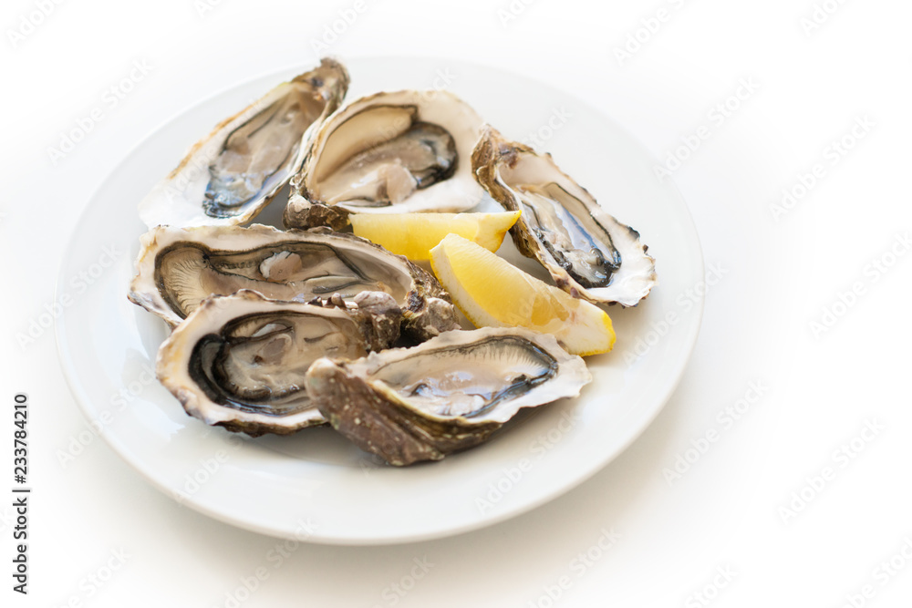 Fresh oysters. Raw fresh oysters on white round plate, image isolated, with soft focus. Restaurant delicacy. Saltwater oysters Fresh oysters. Raw fresh oysters on white round plate, image isolated, with soft focus. Restaurant delicacy. Saltwater oysters