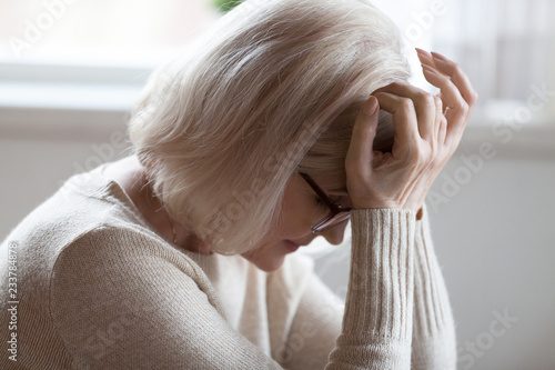 Fotografie Tired elderly woman suffer from severe headache sitting with eyes closed, exhaus