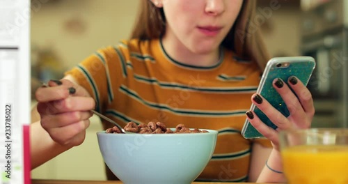 Teenage Girl Eating Unhealthy Bowl Of Sugary Breakfast Cereal Texting On Mobile Phone