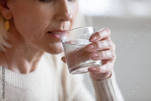 Aged woman holding glass feeling thirsty or dehydrated, senior female drinking fresh pure aqua following healthy lifestyle, elderly lady having still mineral water. Refreshment, dehydration concept photo