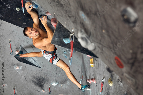 Athletic shirtless man hanging on hands at an indoor climbing centre. Professional climber climbing wall upside down at an indoor climbing gym.