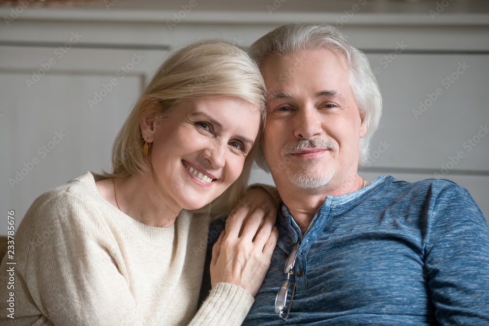 Portrait of smiling senior husband and wife hugging posing for family picture, happy aged couple embrace looking at camera enjoying weekend at home together. Elderly love, relationships goal concept Portrait of smiling senior husband and wife hugging posing for family picture, happy aged couple embrace looking at camera enjoying weekend at home together. Elderly love, relationships goal concept