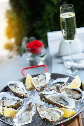 Fresh oysters with lemon's slices in ice and champagne. Restaurant delicacy, beautiful table setting. Saltwater oysters dish. Romantic dinner in restaurant.