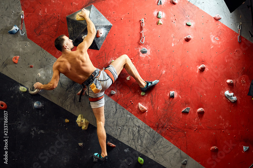 Sporty active businessman engaged in his hobby-bouldering. Equipped with belay system male athlete training in a colorful climbing gym, preparing to summer mountain ascend
