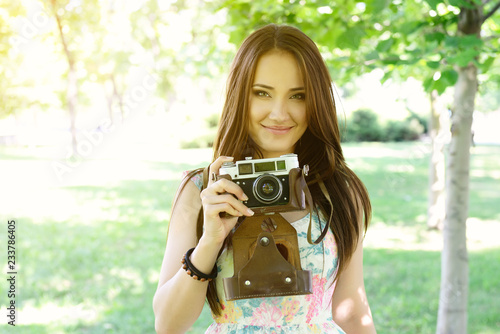 Cheerful beautiful girl talking pictures with vintage camera in summer park