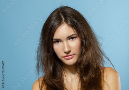 Beautiful calm teen girl looking at camera over blue background. Young woman posinng at studio.