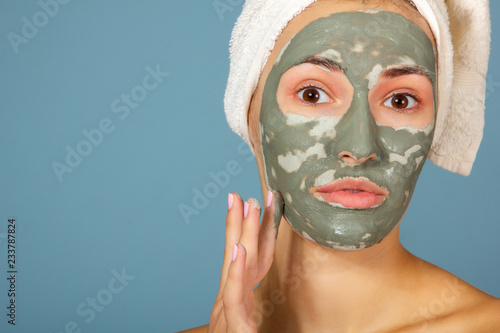 Beautiful cheerful teen girl applying facial clay mask. Beauty treatments, isolated on blue background.