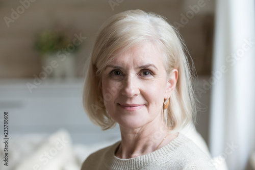Close up portrait of happy aged beautiful female looking at camera relaxing at home, smiling senior woman posing for picture or photo, elderly lady feeling positive shoot for album in country house