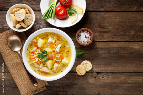 Chicken soup with noodles and vegetables in white bowl on wooden background