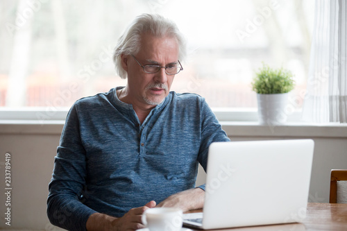 Confused senior male use laptop looking at screen shocked by received message or letter, stunned aged man frustrated by unexpected bad news online, disappointed elderly get negative response in email