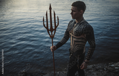 A young man with a trident against the background of water.