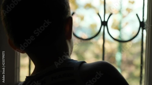 The boy is 3-5 years old outside the window with a lattice