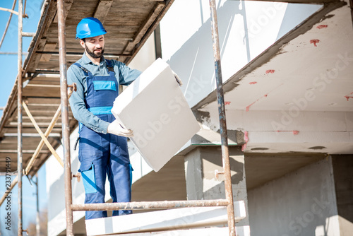 Fotografie Builder warming a building facade with foam panels standing on the scaffoldings