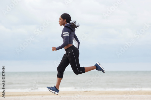 side portrait of sporty young black woman running by the beach