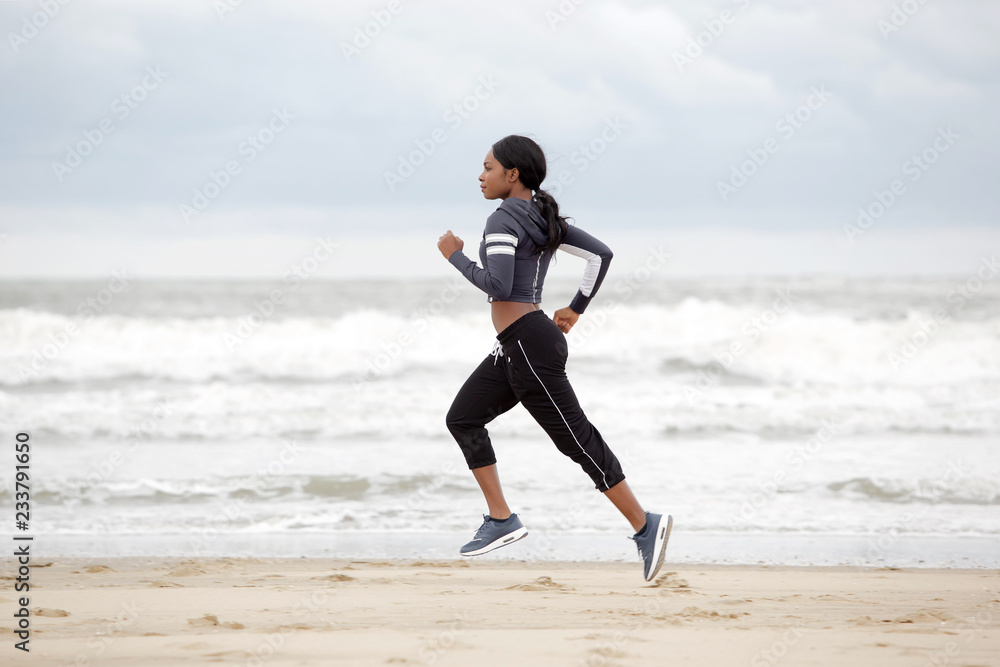 Full length young african american woman running on the beach by the water Full length young african american woman running on the beach by the water