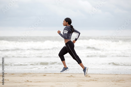 Full length young african american woman running on the beach by the water