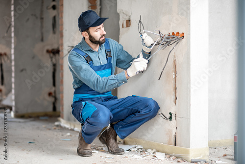 Electrician mounting wiring for electric sockets on the construction site of a new building indoors