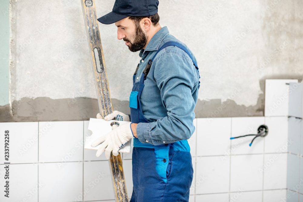 Workman in blue uniform installing white ceramic tiles at the bathroom Workman in blue uniform installing white ceramic tiles at the bathroom