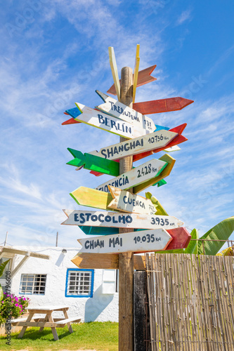 wooden pole guidepost with multiple destinations of the world on arrows sticks (white, yellow, red and green), in Spanish: Berlin, Shanghai, Florence, Stockholm, Chiang Mai, Trebujena and Cuenca photo