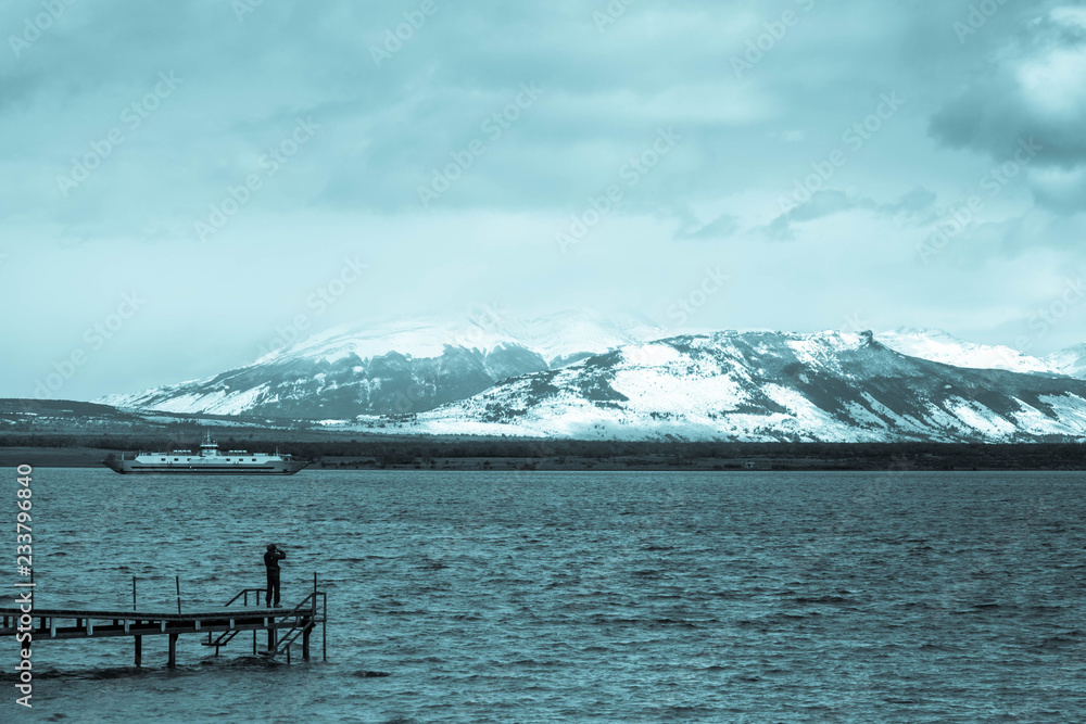 Person on the pier of Puerto Natales, Patagonia, Chile, watching the fjord 'Última Esperanza' and the mountains.
