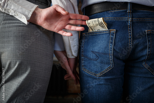 Rear View Of young couple holding hands, the second hand wife pulls money from the pocket of her husband's denim trousers until he sees