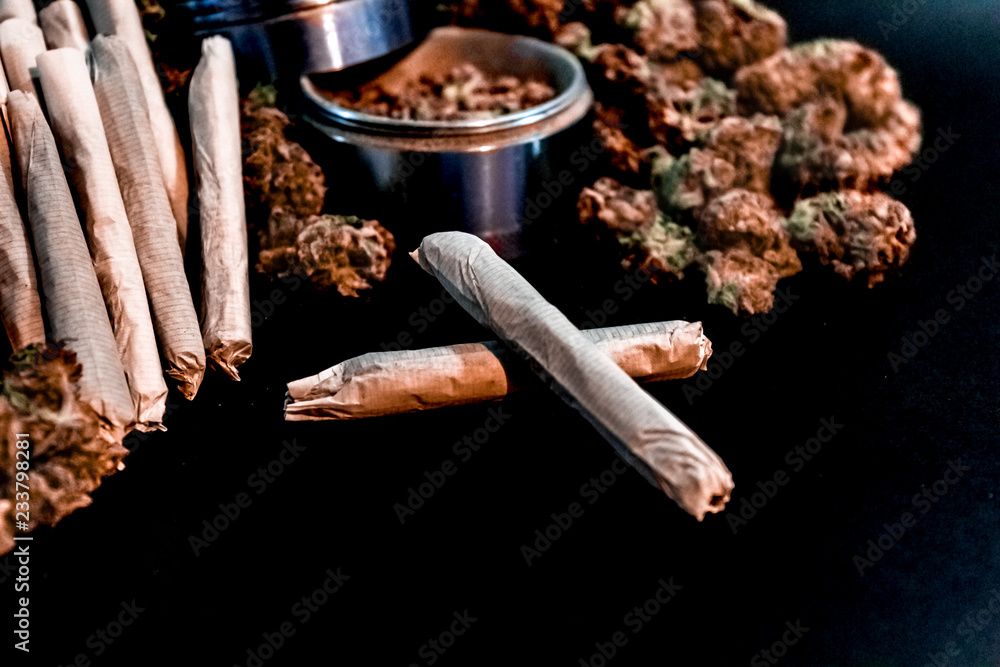 Marijuana joints surrounded by a large pile of bud and a bud grinder.