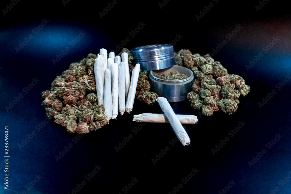 Marijuana joints stacked on a pile of bud with a blue coloured bud grinder.