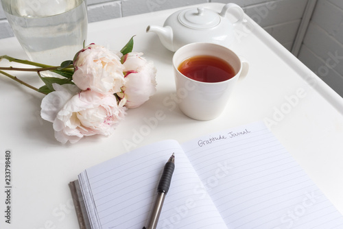 Картината върху платно Closeup of gratitude journal on white table with peonies, cup of tea and teapot