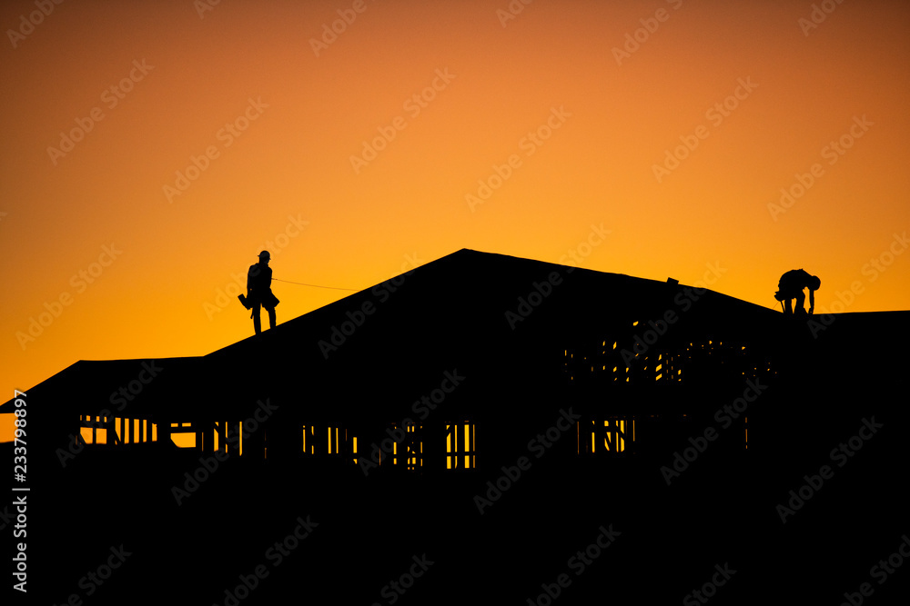 Silhouette of builders working on new construction home during sunset