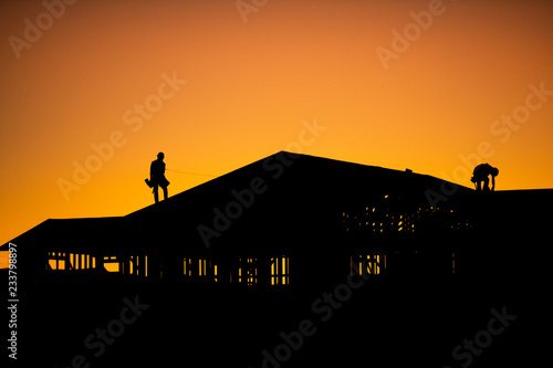 Silhouette of builders working on new construction home during sunset