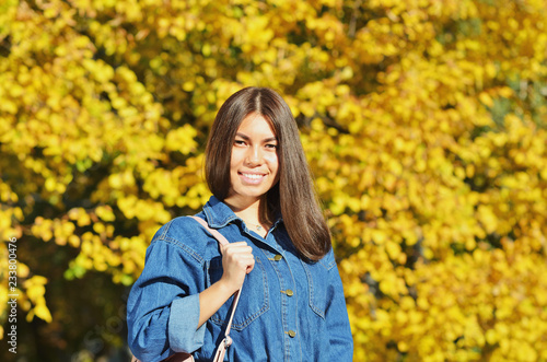 A young girl stands on a background of yellow leaves in city Park