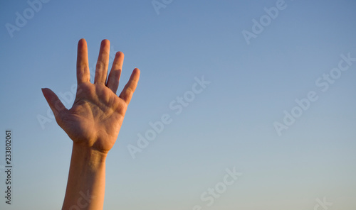 Woman's hand isolated on blue background in summer sky nature. Stop, help, fifth concept with hand up. Gesture symbol number five in sign language. Say hello / hi or goodbye concept with copy space.