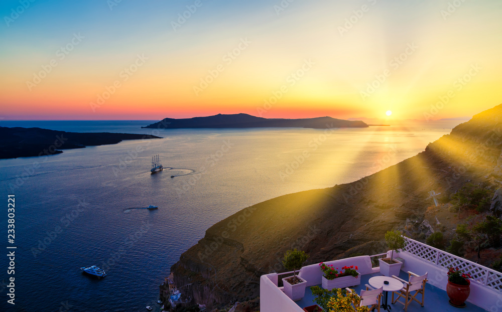 Fototapeta sun's rays cut through slope and illuminate terrace of the bay of Santorini, with the ship in the background and the caldera