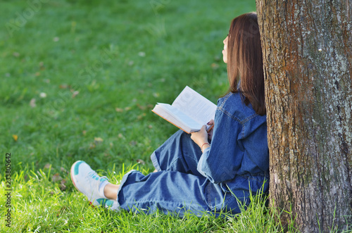 Young pretty student woman is sitting near the tree with a book