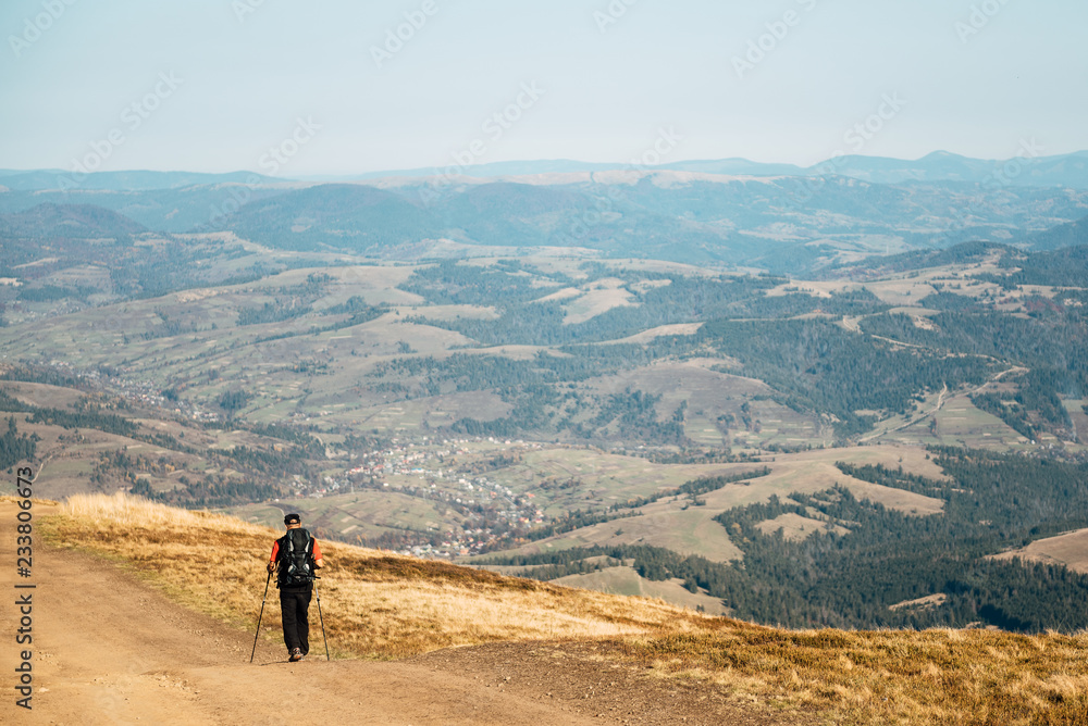 Man traveler walking along the road. There are mountains on the horizon. The sky is blue and cloudy.