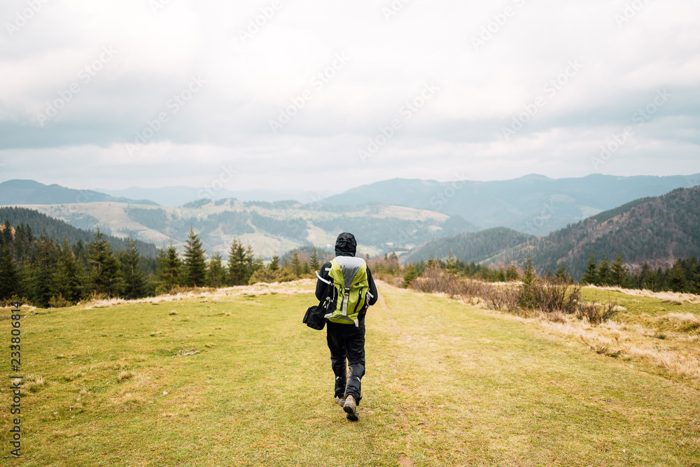 Obraz premium Man with a backpack walking along the road. There are mountains on the horizon. The sky is blue and cloudy.