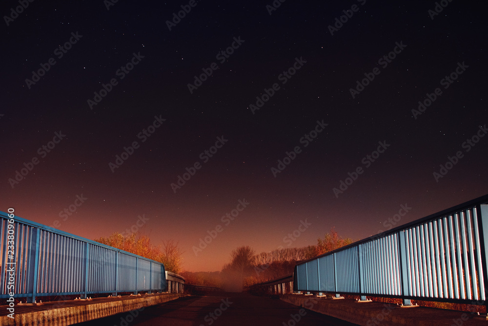 Night view from a bridge with blue rails and night star view with a road leading to foggy nature landscape. Braunschweig, Germany