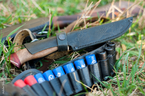 A hunting knife, a gun, a cartridge belt lie on the ground.