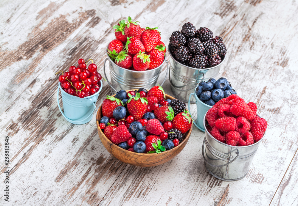 Berries fresh colorful arrangement in tin cans and wooden bowl on old white rustic wooden table front view studio shot Berries fresh colorful arrangement in tin cans and wooden bowl on old white rustic wooden table front view studio shot