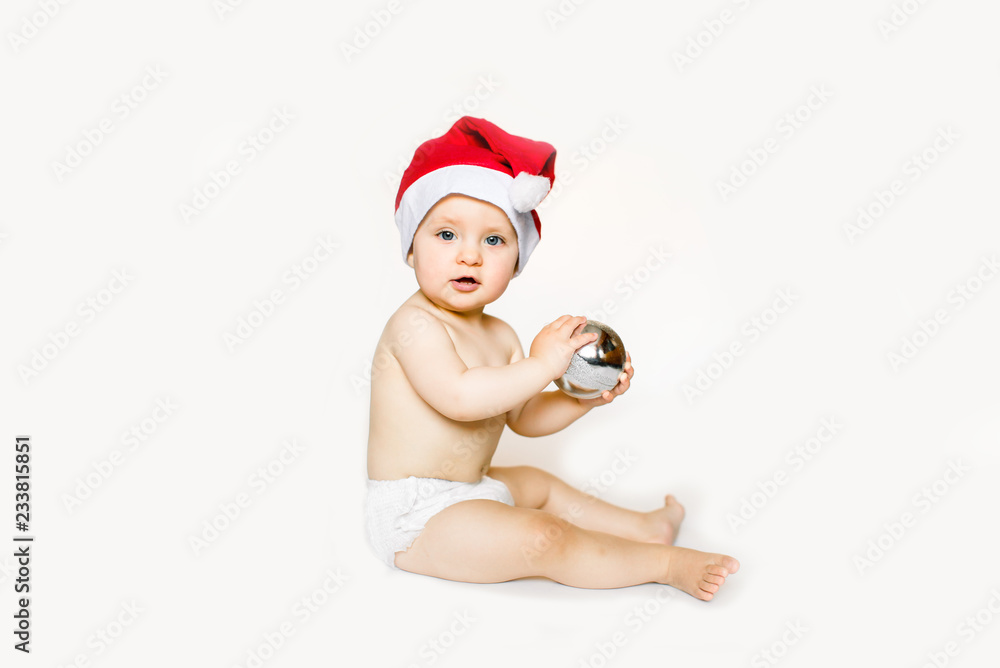 Happy baby in a Christmas costume Santa Claus with christmas ball on white brick wall Happy baby in a Christmas costume Santa Claus with christmas ball on white brick wall