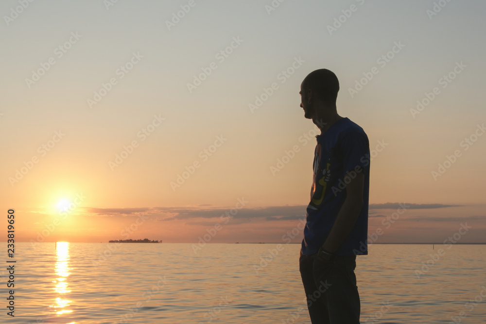 a young man stands on the beach and watches a beautiful sunset over the sea, a red sunset. warm countries.